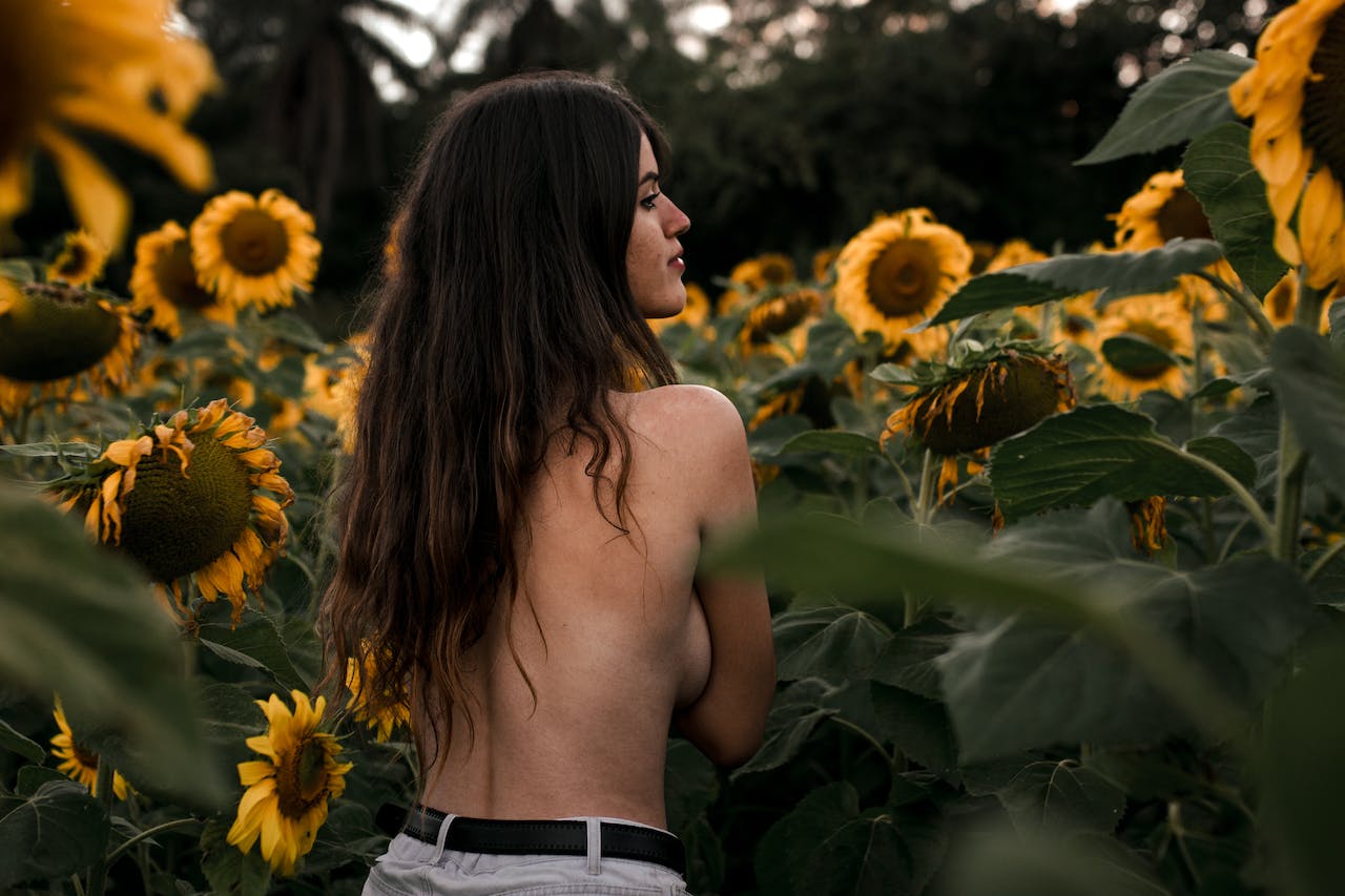 shirtless woman sorrounded by sunflowers