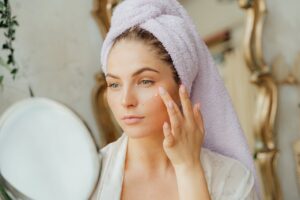 woman with head towel applying face cream