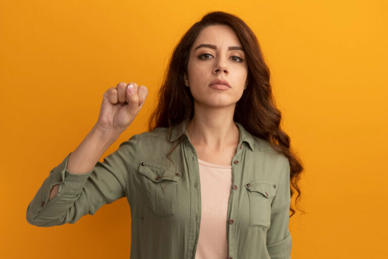 confident young beautiful girl wearing olive green t shirt holding fist isolated yellow wall