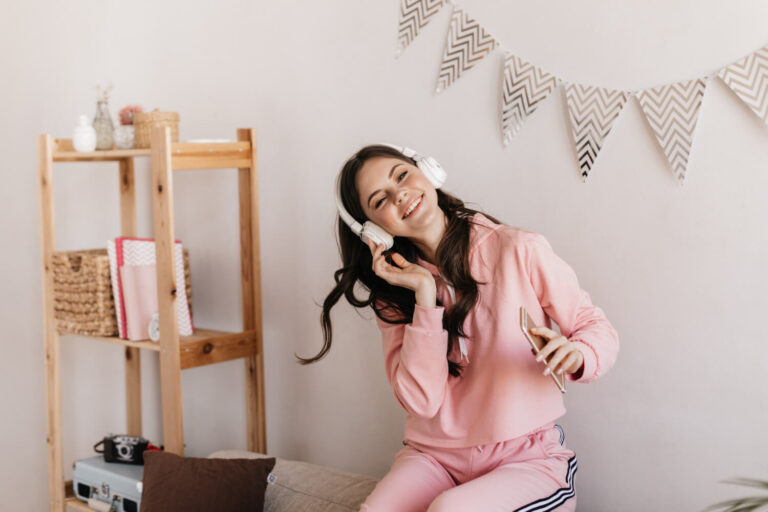 curly woman white headphones looks front with smile holds phone enjoys music