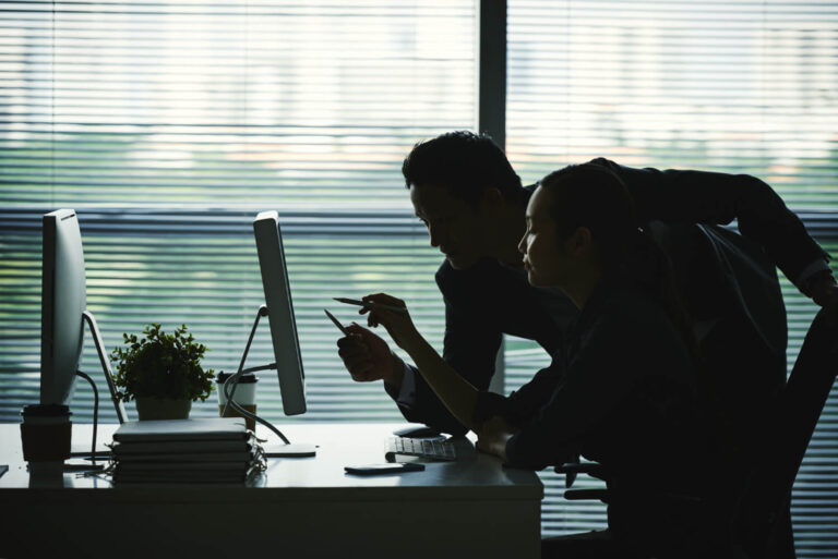 dark silhouettes colleagues pointing computer screen office against window