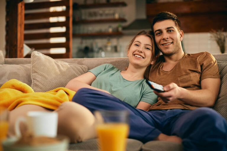 happy couple watching movie while relaxing sofa home