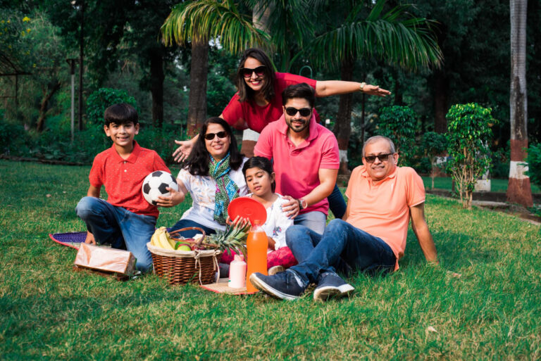 Indian family enjoying picnic multi generation asian family sitting lawn green grass park with fruit basket mat drinks selective focus