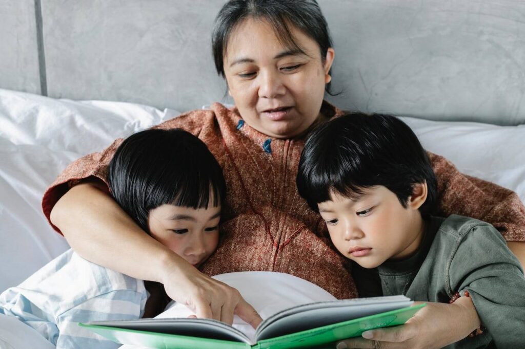 ethnic mother and little kids reading book in bed