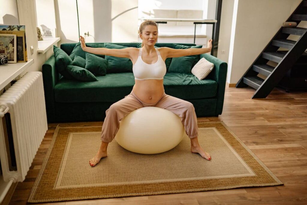 a pregnant woman sitting on a yoga ball with arm stretched