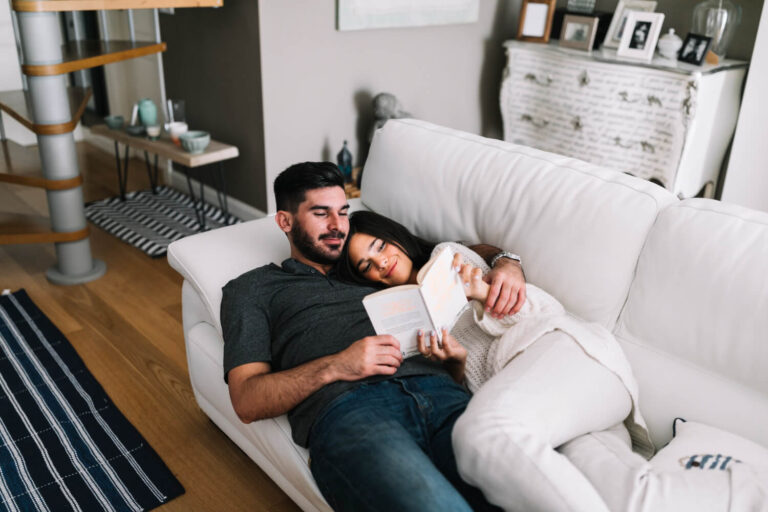 smiling young couple lying sofa reading book living room