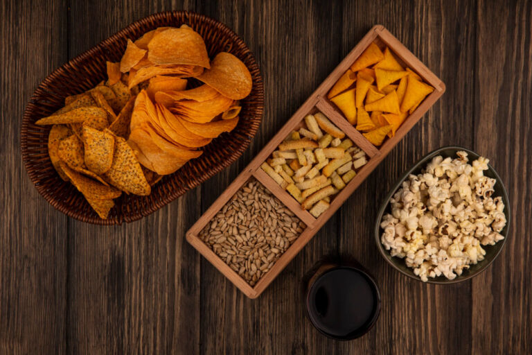 top view cone shape corn snacks wooden divided plate with shelled sunflower seeds with spicy chips bucket with glass cola wooden table