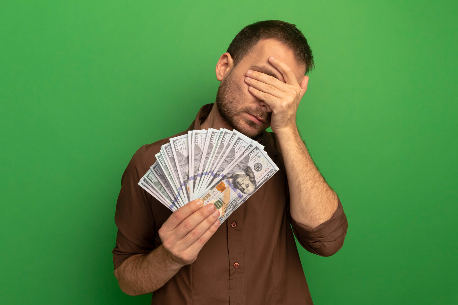 young Caucasian man holding money covering eyes to stop spending money
