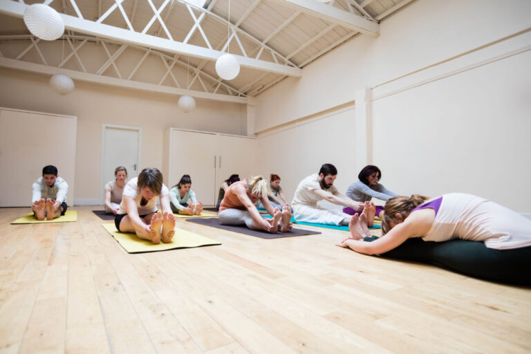 trainer assisting group people with pashimottanasana exercise