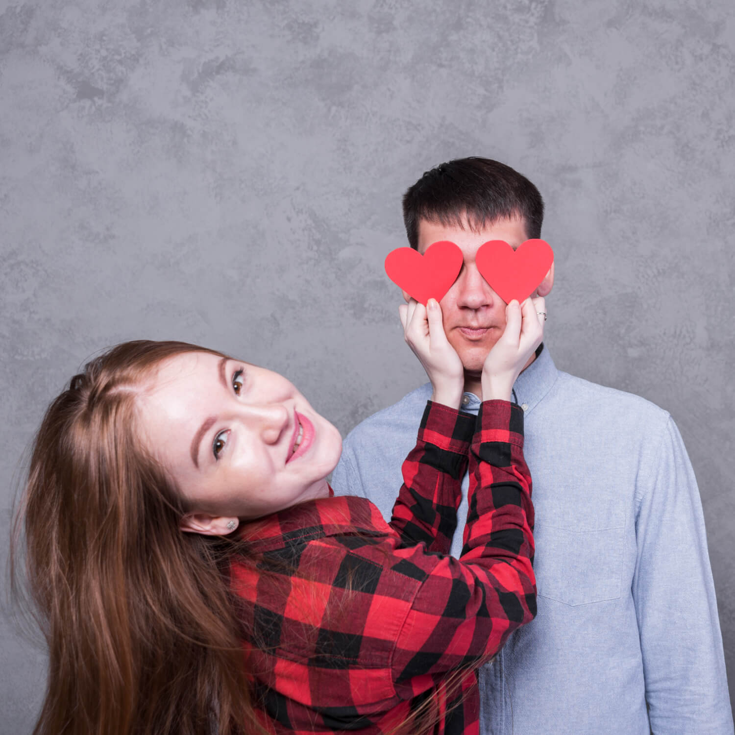 woman smiling covering man eyes with paper hearts