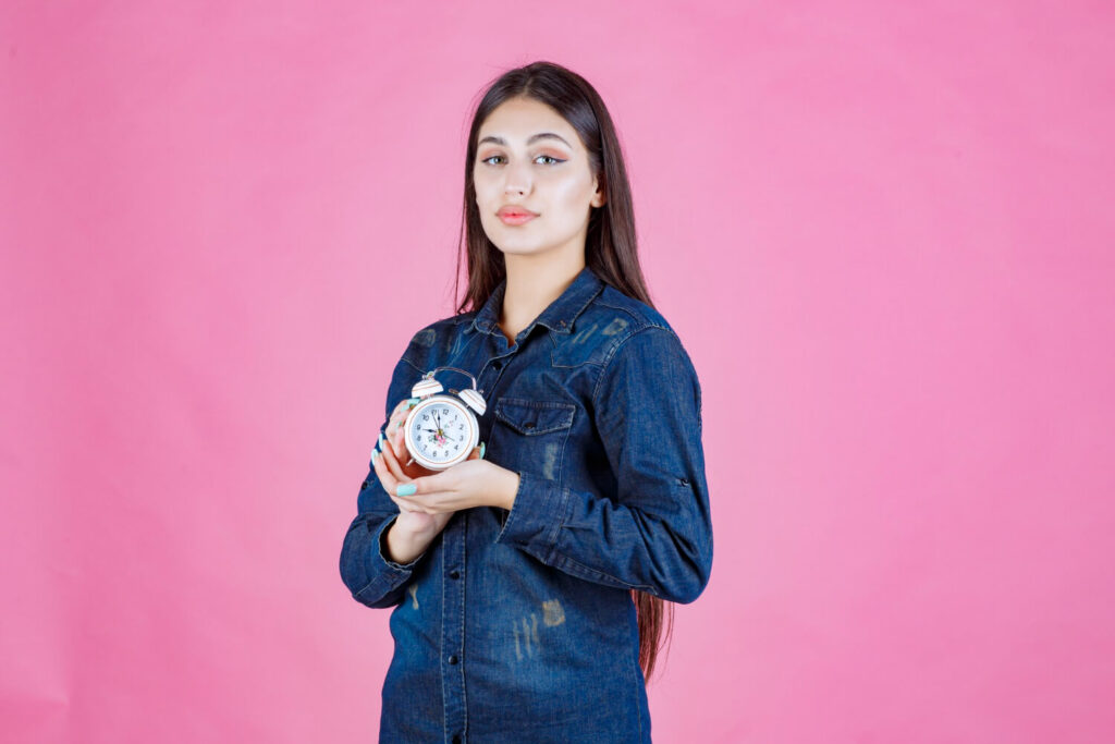 young woman denim shirt holding alarm clock her hands