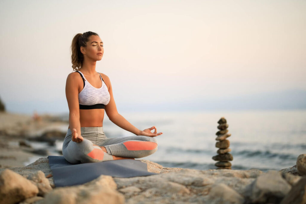 young woman practicing yoga relaxation exercises meditating rock beach copy space