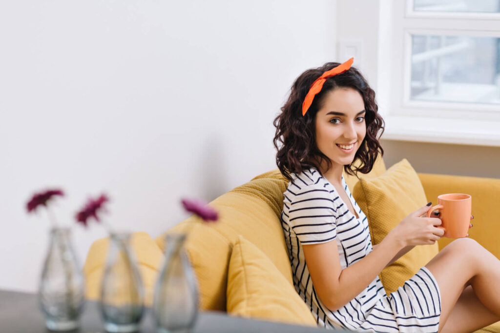 charming young woman dress smiling couch modern apartment orange white golden colors cheerful mood smiling resting relaxing