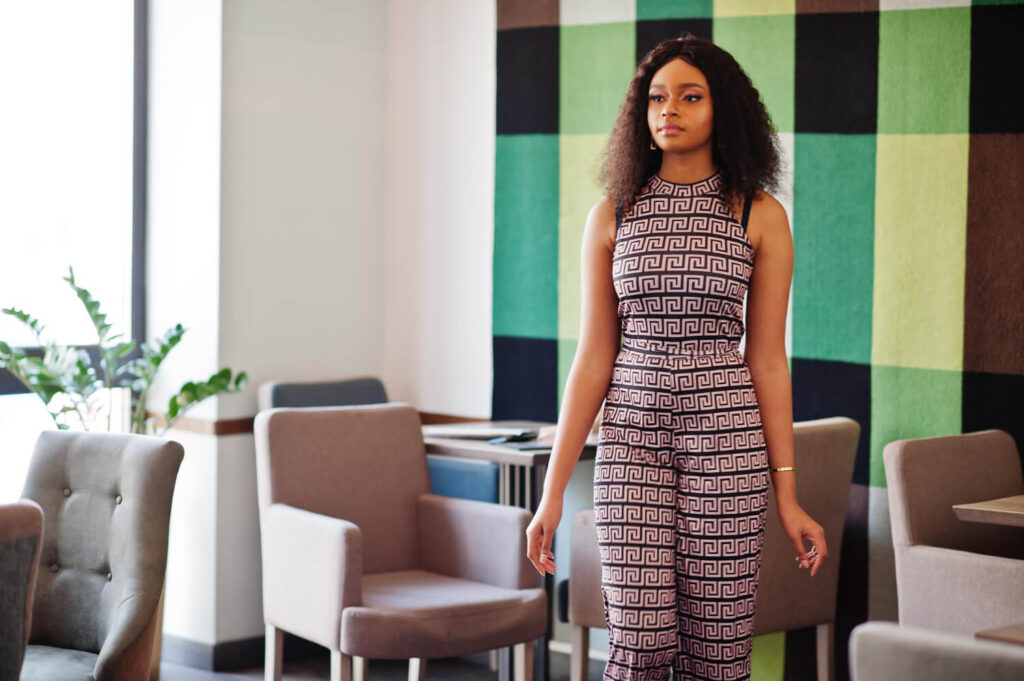 sharming elegant young african american woman with long curly hair wearing jumpsuit posing cafe indoor