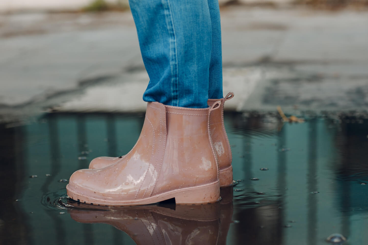 woman wearing rain rubber boots walking running jumping into puddle with water splash drops autumn rain
