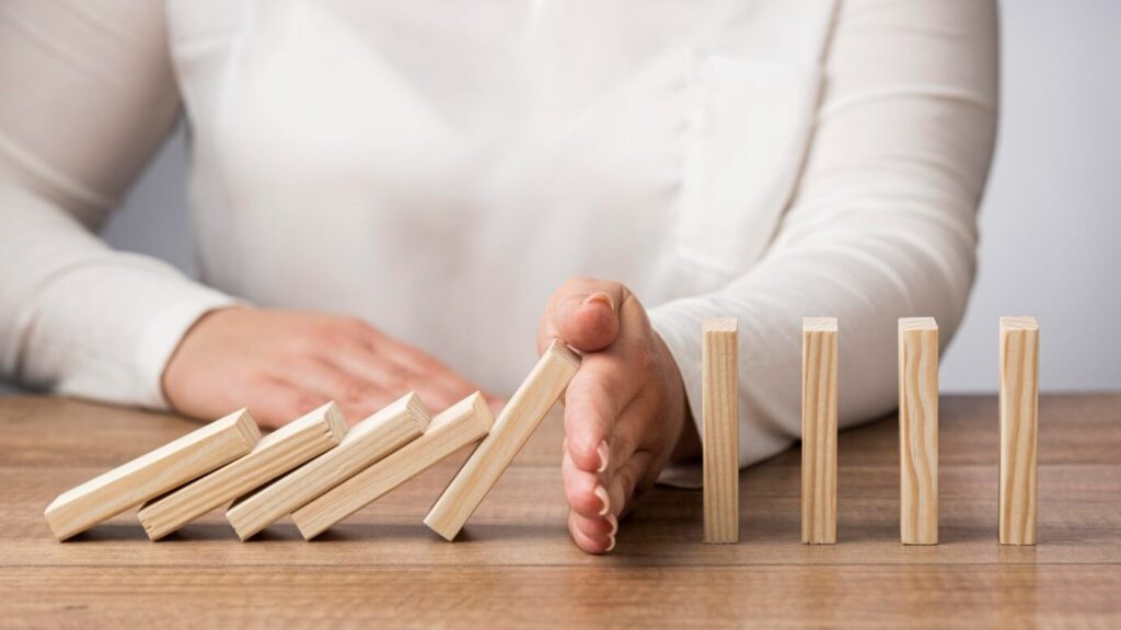 A person in a white shirt preventing a row of dominoes from falling over.