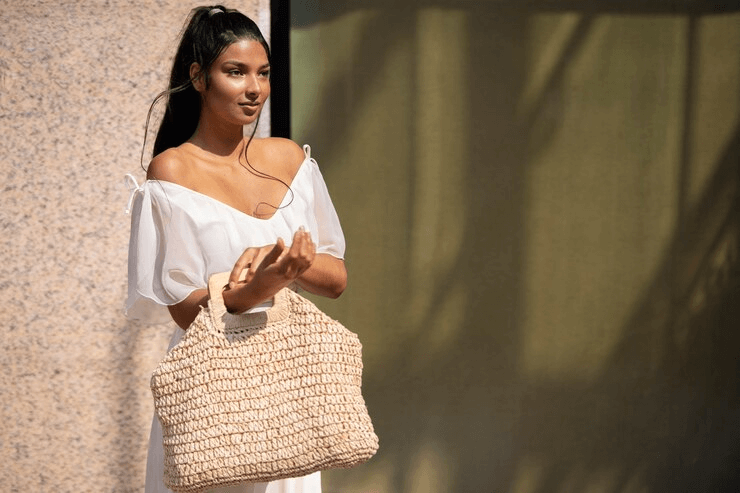 A woman in a white dress elegantly holds a straw bag, exuding a sense of style and sophistication