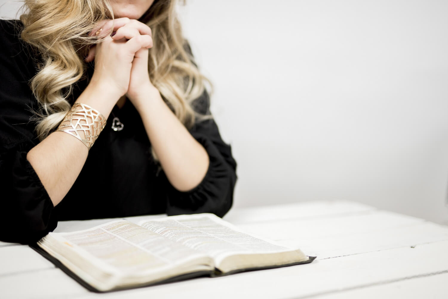 Woman praying with tightly linked fingers near open book table